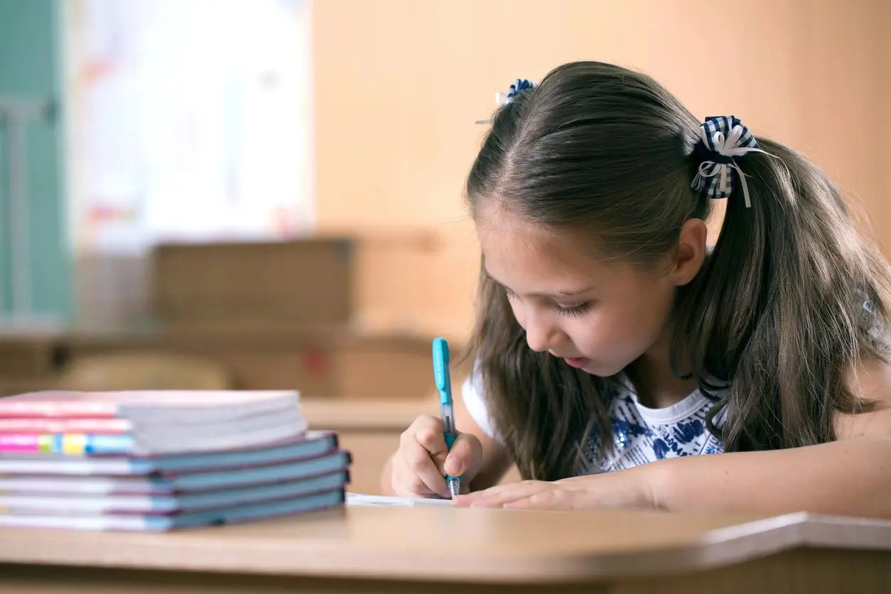A small kid writing something with her pen sitting at a desk